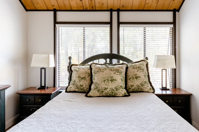 A bedroom with a green wooden bed frame, white bedding, and exposed beams