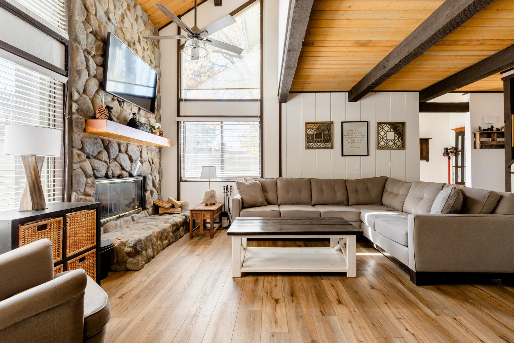 Sunlit living room with exposed wooden beams, a stone fireplace, and a sofa